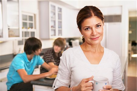 Mother in Kitchen With Cup of Coffee, Sons Eating Breakfast in the Background Foto de stock - Con derechos protegidos, Código: 700-02738786