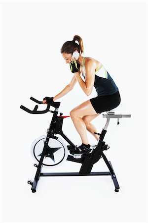 Woman Talking on Cell Phone While Riding Stationary Bicycle Foto de stock - Con derechos protegidos, Código: 700-03004417