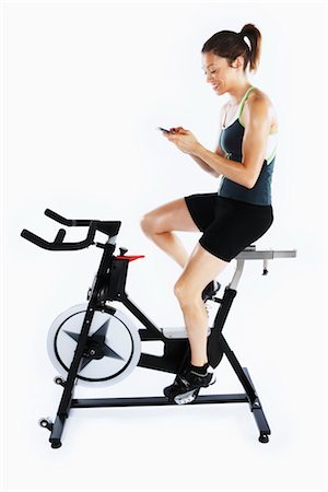 spinning - Woman Using Cell Phone While Riding Stationary Bicycle Foto de stock - Con derechos protegidos, Código: 700-03004418