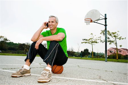 Homme à l'aide de téléphone portable sur le terrain de basket Photographie de stock - Rights-Managed, Code: 700-03519163