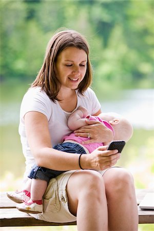 Femme avec téléphone cellulaire à l'aide de bébé Photographie de stock - Rights-Managed, Code: 700-03778075