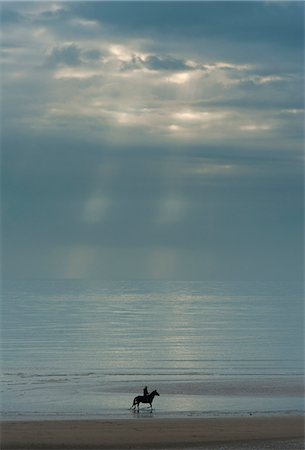 raining on the beach photos - Person riding horse along Camber Sands on cloudy day with rays of sunshine; East Sussex, England Stock Photo - Rights-Managed, Code: 832-08007559