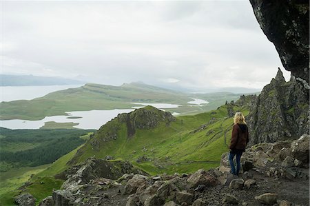 A woman stands along on a rocky ridge looking out over the landscape of hills and water; Skye, Scotland Foto de stock - Direito Controlado, Número: 832-08007787