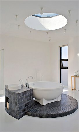 Salle de bains, avec un puits de lumière circulaire qui permet à la lumière d'inonder vers le bas sur la baignoire circulaire et son socle de brique. Maison d'un collectionneur d'art dans la banlieue nord de Beijing. Conçu par l'artiste voisin Shao Fan, qui a également conçu les meubles, cela fait partie d'un composé de plusieurs amis. Photographie de stock - Rights-Managed, Code: 845-05838380