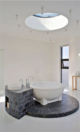 fuente (origen) - Bathroom, with a circular skylight that allows light to flood down onto the circular bath and its brick plinth. House of an art collector on the northern outskirts of Beijing. Designed by neighbouring artist Shao Fan, who also designed the furniture, this is part of a compound of several friends. Foto de stock - Con derechos protegidos, Código: 845-05838380