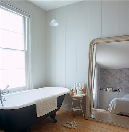 Freestanding roll top bathtub beneath window next to mirror reflecting double bed. Designed by Designed by Clare Nash Stock Photo - Rights-Managed, Code: 845-05838834
