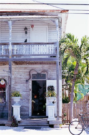 photo picket garden - Two storey clapboard house, painted white, with balcony and verandah, weather beaten, peeling paint, urns containing ferns either side of door, palm tree in garden Foto de stock - Con derechos protegidos, Código: 845-02729320