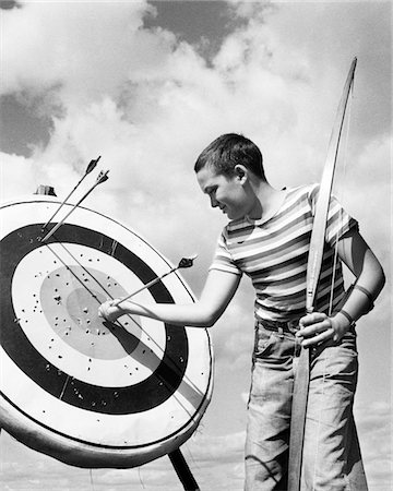 sports 1950s - 1950s BOY JEANS STRIPED T-SHIRT HOLDING BOW & PULLING ARROW OUT OF TARGET BULL'S-EYE Stock Photo - Rights-Managed, Code: 846-05645894