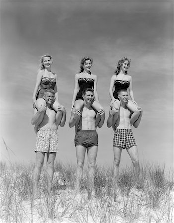 1950s - 1960s THREE COUPLES AT BEACH ON DUNES WITH WOMEN IN IDENTICAL BATHING SUITS SITTING ON MEN'S SHOULDERS Foto de stock - Con derechos protegidos, Código: 846-05645933