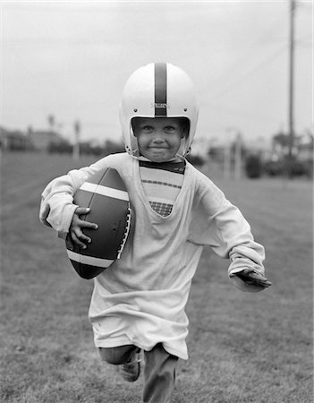 simsearch:846-05648516,k - 1950ER JAHRE BOY IN ÜBERGROßEN SHIRT & HELM LAUFEN IN RICHTUNG KAMERA HOLDING-FUßBALL Stockbilder - Lizenzpflichtiges, Bildnummer: 846-05645945