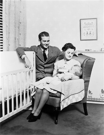 simsearch:846-05645972,k - 1930s - 1940s MOTHER SITTING IN CHAIR IN NURSERY BABY 11 MONTHS ON LAP DRINKING FROM BOTTLE FATHER LOOKING ON LEANING ON CRIB Stock Photo - Rights-Managed, Code: 846-05646125