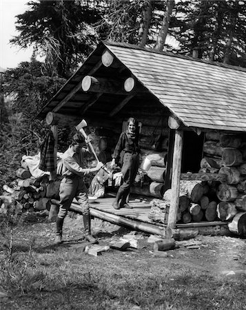 1920s - 1930s COUPLE WOMAN STANDING ON PORCH OF LOG CABIN HOLDING PITCHER MAN CHOPPING WOOD ASSINIBOINE CANADA Stock Photo - Rights-Managed, Code: 846-05646204