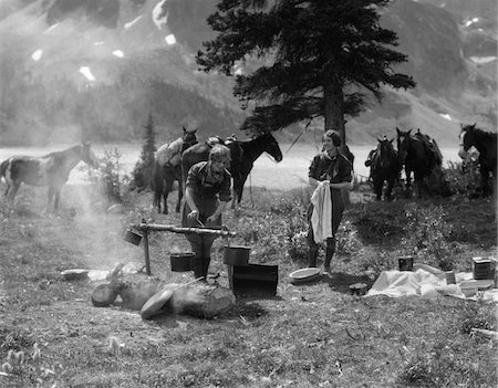 ANNÉES 1920 - ANNÉES 1930, DEUX FEMMES AU CAMPING FEMME CUISSON PRÉPARATION ALIMENTAIRE À CHEVAUX DE FEU DE CAMP AVEC RIDING GEAR EN ARRIÈRE-PLAN Photographie de stock - Rights-Managed, Code: 846-05646200