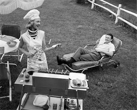 retro women camping - 1950s - 1960s WOMAN IN CHEF'S HAT AND APRON GRILLING HOT DOGS ON GRILL MAN IN CHAISE LONGUE LAUGHING EATING A FRANKFURTER OUTSIDE Stock Photo - Rights-Managed, Code: 846-05646226