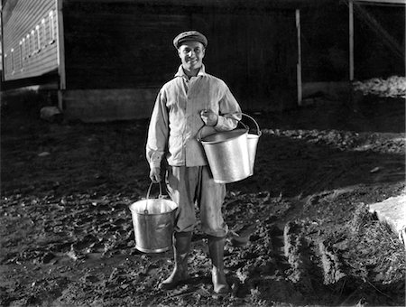 farmers with dairy cows - 1930s - 1940s MAN FARMER DAIRYMAN STANDING OUTSIDE BARN HOLDING MILK PAILS WEARING CAP JACKET RUBBER KNEE BOOTS SMILING LOOKING AT CAMERA Stock Photo - Rights-Managed, Code: 846-05646261