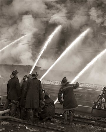 1950s FIREMEN USING WATER HOSES ON SMOKING BURNING BUILDING TO EXTINGUISH FIRE Stock Photo - Rights-Managed, Code: 846-05646349