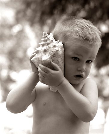 1960s BOY TODDLER HOLDING SEASHELL TO EAR LISTENING TO OCEAN SOUNDS SUMMER BEACH Stock Photo - Rights-Managed, Code: 846-05646486