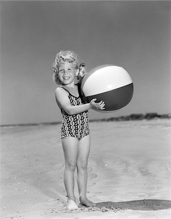 ANNÉES 1950 JEUNE FILLE SOURIANTE DEBOUT SUR LE BALLON DE PLAGE DE TENUE DE PLAGE REGARDANT LA CAMÉRA Photographie de stock - Rights-Managed, Code: 846-05646533