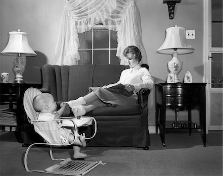 pessoa cuidando do bebê - 1950s TEEN BABYSITTER SEATED ON SOFA READING SCHOOLBOOK WHILE BABY IN BOUNCY SLING CHAIR GRABS HER PROPPED UP FOOT Foto de stock - Direito Controlado, Número: 846-05646550