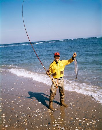 1970s MAN RED CAP HAT YELLOW SHIRT WADERS ON BEACH SURF FISHING HOLDING UP CATCH OF THE DAY Foto de stock - Con derechos protegidos, Código: 846-05646598