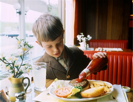 salsa de tomate - 1960s BOY EATING AT BOOTH IN RESTAURANT POURING KETCHUP ON HAMBURGER Foto de stock - Con derechos protegidos, Código: 846-05646844
