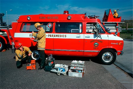 1970s - 1980s TWO MEN PARAMEDIC TEAM INSPECTING CHECKING EQUIPMENT AT AMBULANCE VAN WEARING FIREMEN HELMETS JACKETS Stock Photo - Rights-Managed, Code: 846-05646862
