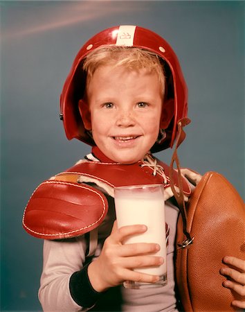 1960ER JAHRE BLONDEN JUNGEN LÄCHELND RED HELM TRAGEN FUßBALL SCHULTERPOLSTER HALTEN GLAS MILCH & FUßBALL Stockbilder - Lizenzpflichtiges, Bildnummer: 846-05646897