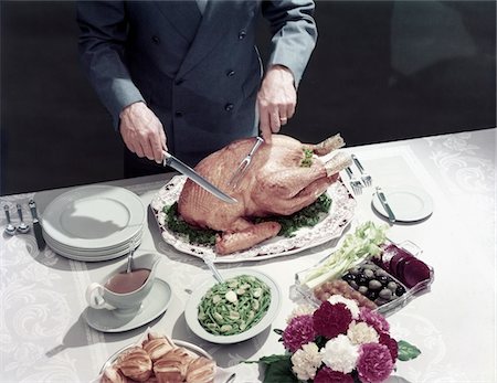 1950s MALE HANDS ABOUT TO CARVE THANKSGIVING TURKEY TABLE SETTING PLATES GRAVY ROLLS OLIVES CRUDITES Fotografie stock - Rights-Managed, Codice: 846-05646943