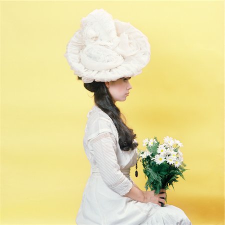 1960s GLAMOUR WOMAN IN WHITE 1890s - 1900s TURN OF THE 19TH CENTURY HAT AND CLOTHES HOLDING FLOWERS SITTING IN PROFILE Foto de stock - Con derechos protegidos, Código: 846-05646975