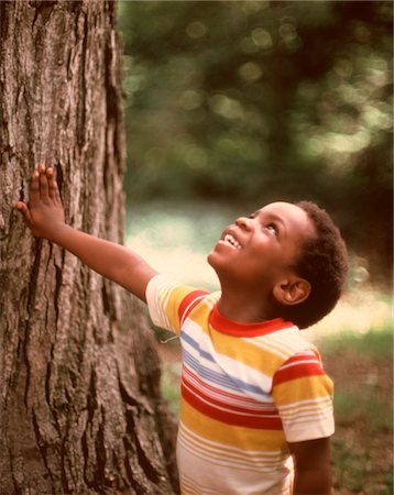 DES ANNÉES 1970 GARÇON AFRO-AMÉRICAIN SOURIRE LEVANT LE TRONC DE L'ARBRE PORTANT TEE-SHIRT RAYÉ Photographie de stock - Rights-Managed, Code: 846-05647161