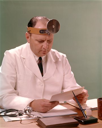 simsearch:400-03924532,k - 1960s MAN DOCTOR SEATED AT DESK READING PAPERWORK Stock Photo - Rights-Managed, Code: 846-05647199