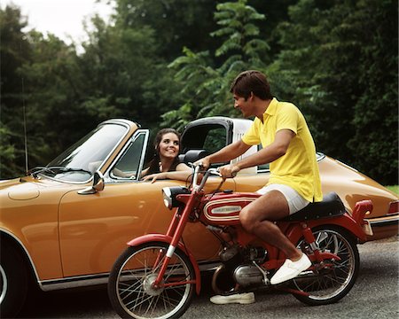 simsearch:846-05647208,k - 1970s LIFESTYLE TALKING FLIRT COUPLE MAN ON SMALL RED HARLEY DAVIDSON MOTORCYCLE SMILING WOMAN IN ORANGE PORSCHE AUTOMOBILE Stock Photo - Rights-Managed, Code: 846-05647208