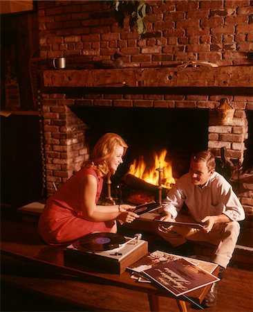 people listening to music 1960s - 1960s - 1970s COUPLE MAN WOMAN BY LIVING ROOM FIREPLACE PLAYING VINYL RECORD ALBUM MUSIC ON HIGH FIDELITY STEREO TURNTABLE Stock Photo - Rights-Managed, Code: 846-05647215