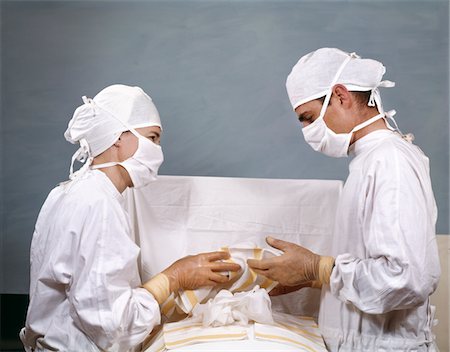 doctor with cap and mask - 1950s - 1960s DOCTOR & NURSE IN SURGERY OPERATION OPERATING STERILE SURGICAL WHITE CAPS GOWNS MASKS Stock Photo - Rights-Managed, Code: 846-05647219