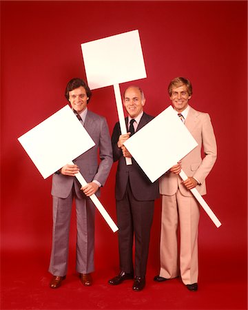 protest - 1970s THREE BUSINESS MEN WEARING SUITS EACH CARRYING BLANK SIGN PLACARD RED BACKGROUND Foto de stock - Con derechos protegidos, Código: 846-05647414