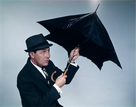 simsearch:846-02794054,k - 1960s BUSINESSMAN WEARING HAT OPENING UMBRELLA TO PROTECT FROM RAIN Stock Photo - Rights-Managed, Code: 846-05647452