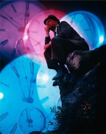 1960s MAN POSED AS THE THINKER ON ROCK WITH HUGE CLOCKS IN BACKGROUND SYMBOLIC TIME PROBLEM LOOMING Stock Photo - Rights-Managed, Code: 846-05647503
