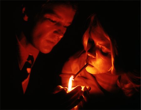 1970s CLOSE-UP OF COUPLE MAN HOLDING FLAME TO LIGHT TOBACCO CIGARETTE FOR WOMAN Fotografie stock - Rights-Managed, Codice: 846-05647514