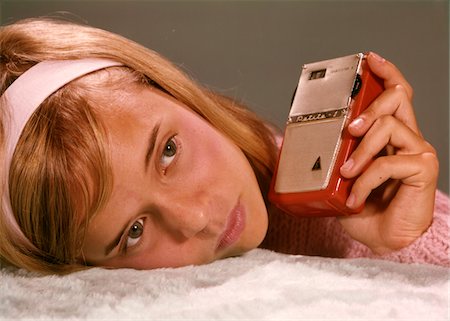 1950s - 1960s TEENAGE GIRL HOLDING RED SILVER SMALL TRANSISTOR RADIO TO HER EAR LISTENING Stock Photo - Rights-Managed, Code: 846-05647529