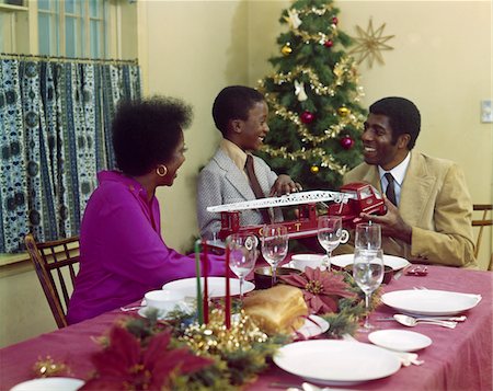 party de noël - ANNÉES 1970 AFRO-AMÉRICAINE FAMILLE MÈRE PÈRE FILS TABLE À MANGER AVEC CAMION DE POMPIER JOUET ARBRE DE NOËL Photographie de stock - Rights-Managed, Code: 846-05647601