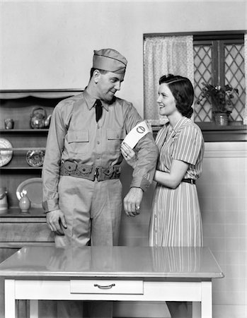 1940s COUPLE MAN WOMAN WIFE HELPING HUSBAND PUT ON CIVIL DEFENSE UNIFORM Foto de stock - Con derechos protegidos, Código: 846-05647662