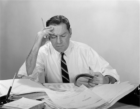 simsearch:846-05646034,k - 1960s BUSINESSMAN DESK FULL PAPERS HAND TO FOREHEAD SERIOUS EXPRESSION Stock Photo - Rights-Managed, Code: 846-05647733