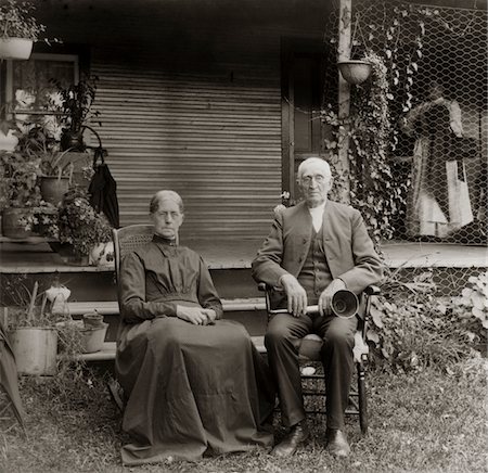 severo - 1890s - 1900s PORTRAIT SENIOR COUPLE SEATED IN GARDEN MAN HOLDING EAR TRUMPET Foto de stock - Direito Controlado, Número: 846-05647767