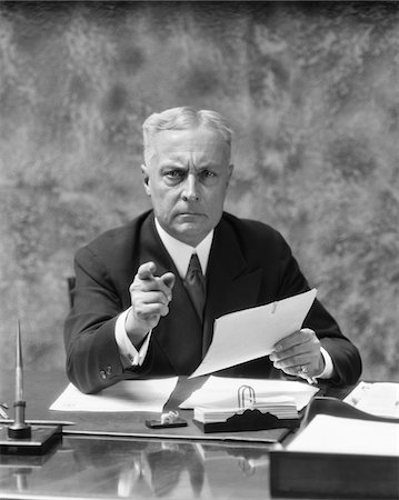 photography portraits in interiors black and white photos - 1930s OLDER MAN SITTING AT DESK IN OFFICE POINTING WITH STERN EXPRESSION Stock Photo - Rights-Managed, Code: 846-05647795