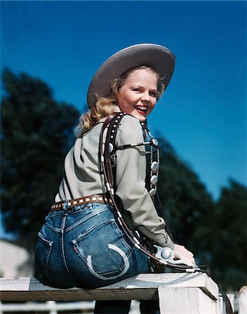 1940s - 1950s SMILING BLOND WOMAN WEARING WESTERN COWGIRL CLOTHES LOOKING OVER SHOULDER SITTING ON WOODEN FENCE Stock Photo - Rights-Managed, Code: 846-05647828