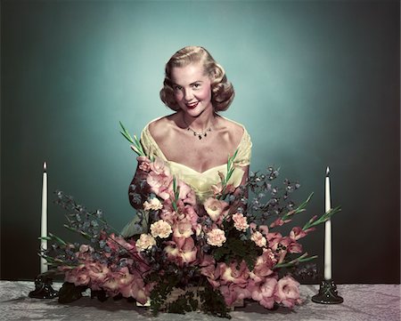 flower arrangement for women - ANNÉES 1950 FEMME SOURIANTE PORTANT ORGANISATION FORMELLE ROBE FLEURS CENTRE DE TABLE SUR TABLE DE SALLE À MANGER Photographie de stock - Rights-Managed, Code: 846-05647846