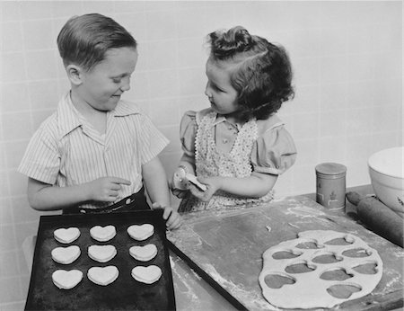 fun black and white photographic images friendship - 1940s YOUNG SMILING GIRL AND BOY BAKING HEART SHAPED VALENTINE COOKIES Stock Photo - Rights-Managed, Code: 846-05648512