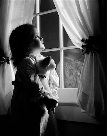 1950s GIRL IN FLANNEL NIGHTGOWN HOLDING STUFFED ANIMAL LOOKING OUT WINDOW AT NIGHT WITH CURTAINS HELD BACK BY HOLLY Foto de stock - Con derechos protegidos, Código: 846-05648532