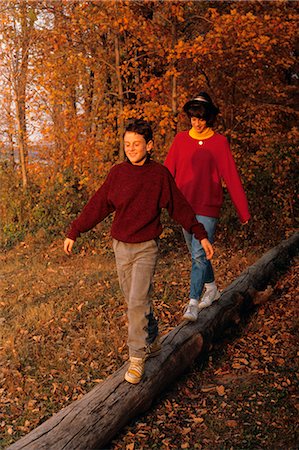 década de 1980 - 1980s BROTHER AND SISTER WALKING ACROSS LOG IN WOODS IN AUTUMN Foto de stock - Direito Controlado, Número: 846-06111726