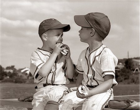 ANNÉES 1960 LITTLE LEAGUE BASEBALL BOYS EN UNIFORMES MANGER DES HOT-DOGS ET DES CASQUETTES Photographie de stock - Rights-Managed, Code: 846-06111777